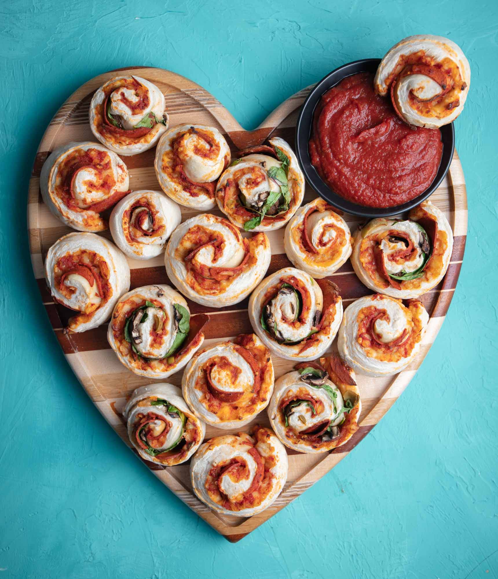 homemade vegan pizza rolls on a heart-shaped cutting board with a side of pizza sauce for dipping
