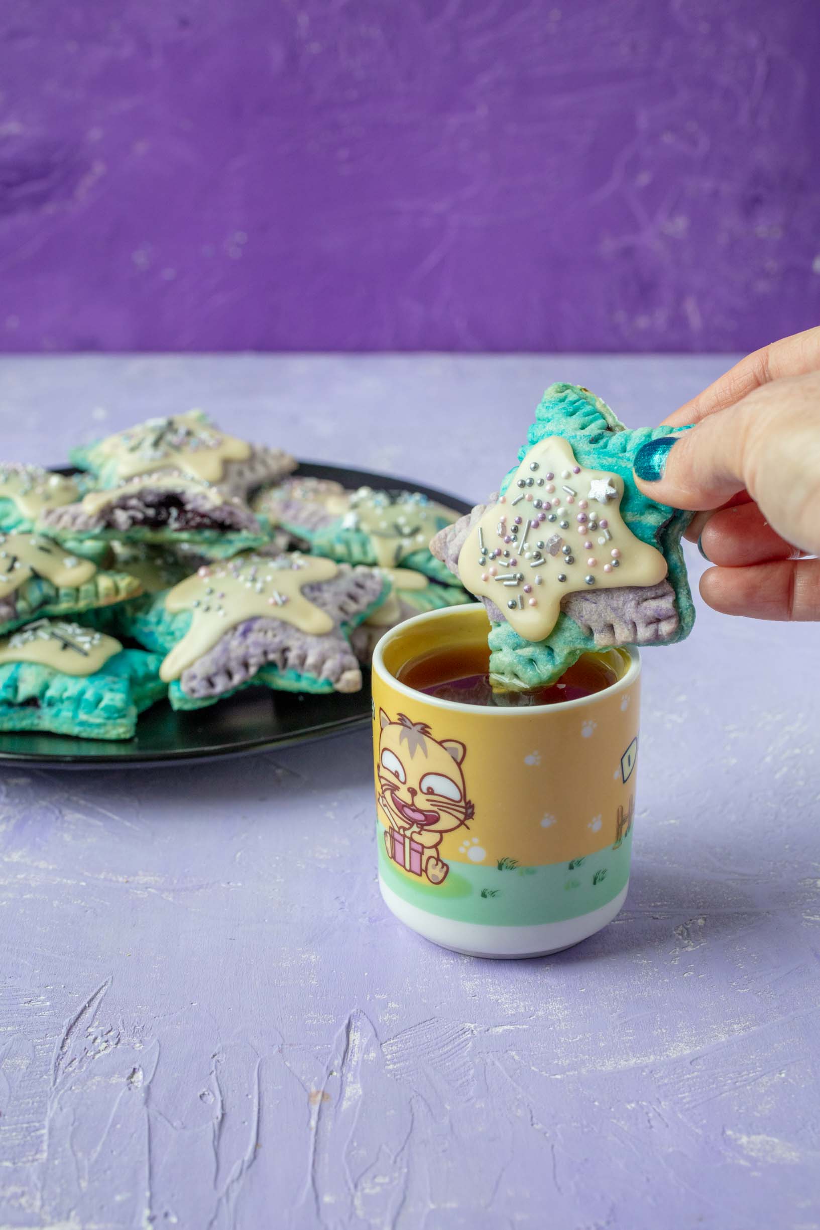 dipping a star shaped poptart into tea with a plate of poptarts in the background.