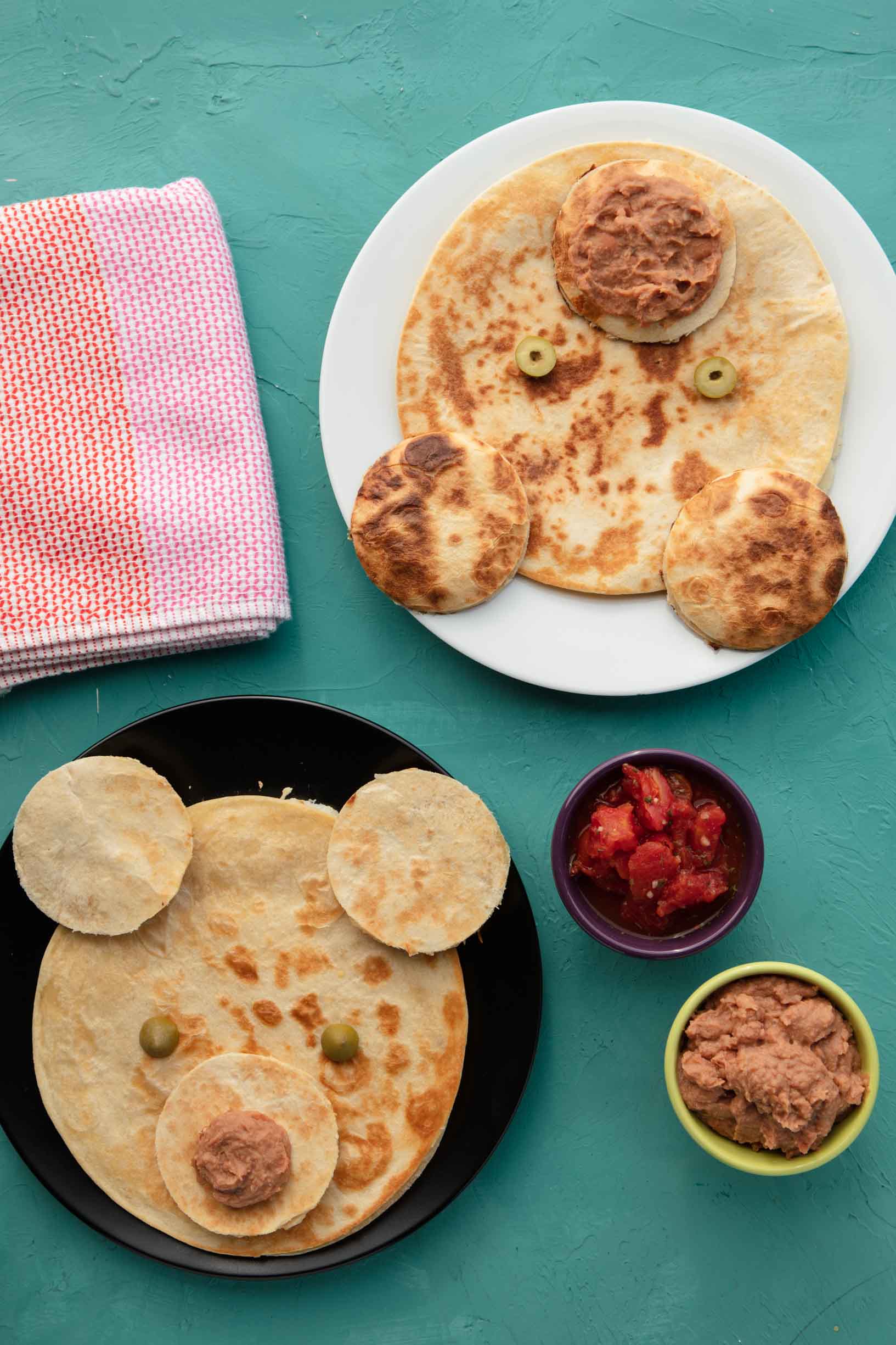 two vegan quesadillas that are decorated like bear faces, served on a table with small bowls of dip