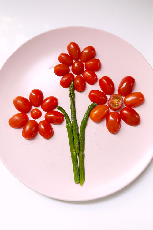 grape tomatoes and roasted asparagus cut in half lengthwise and arranged on a plate to make flowers