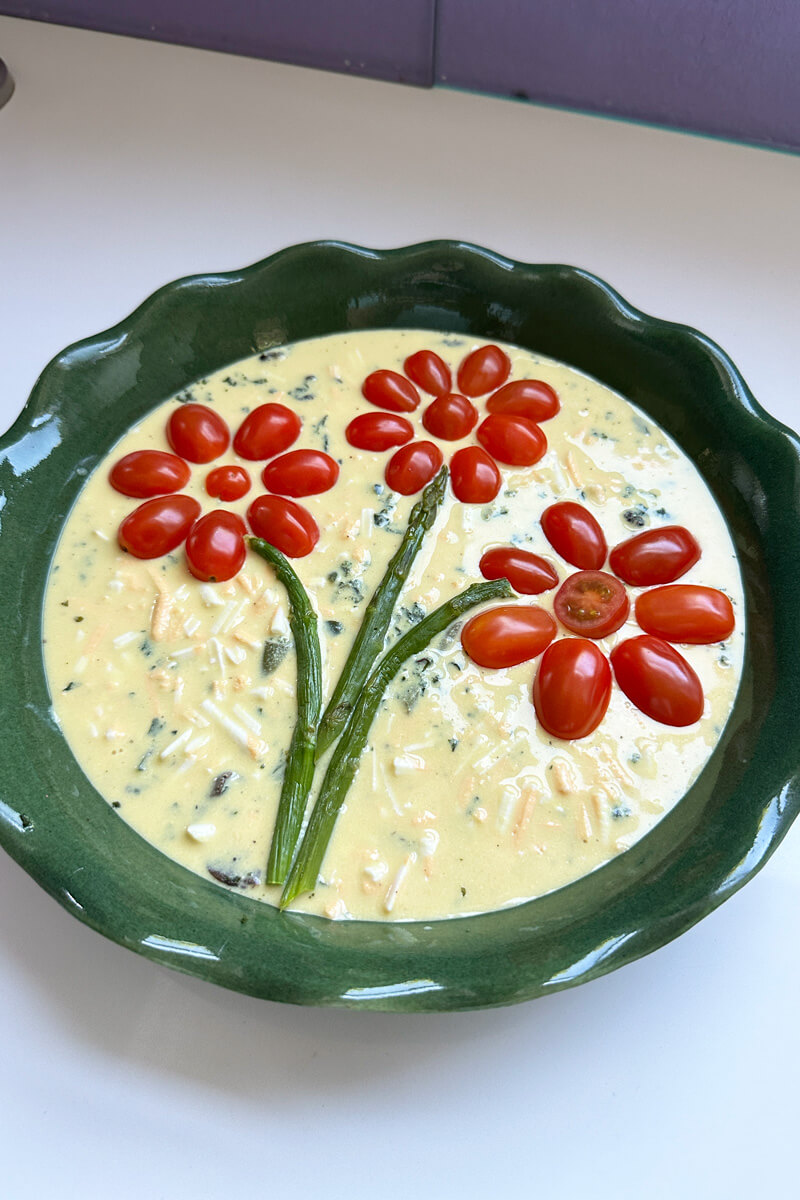 vegan gluten-free quiche decorated with tomato and asparagus flowers on top ready to bake