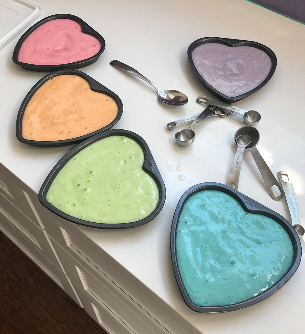 5 heart shaped cake pans filled with 5 different rainbow colors of vegan cake batter