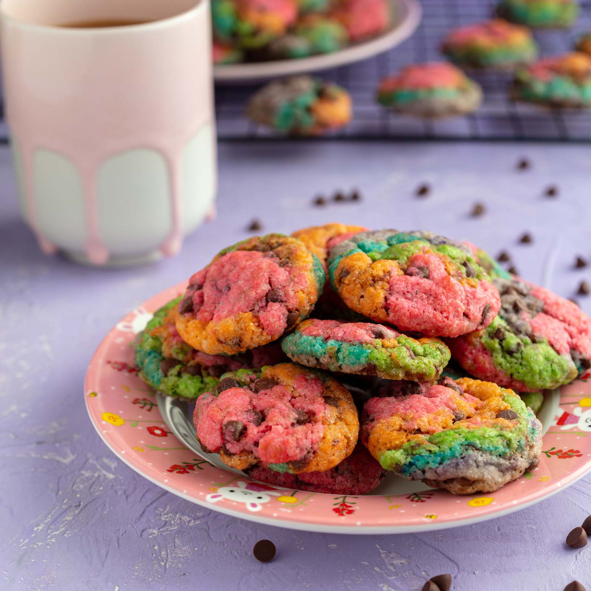 a plate of rainbow chocolate chip cookies with a cup of coffee in the background