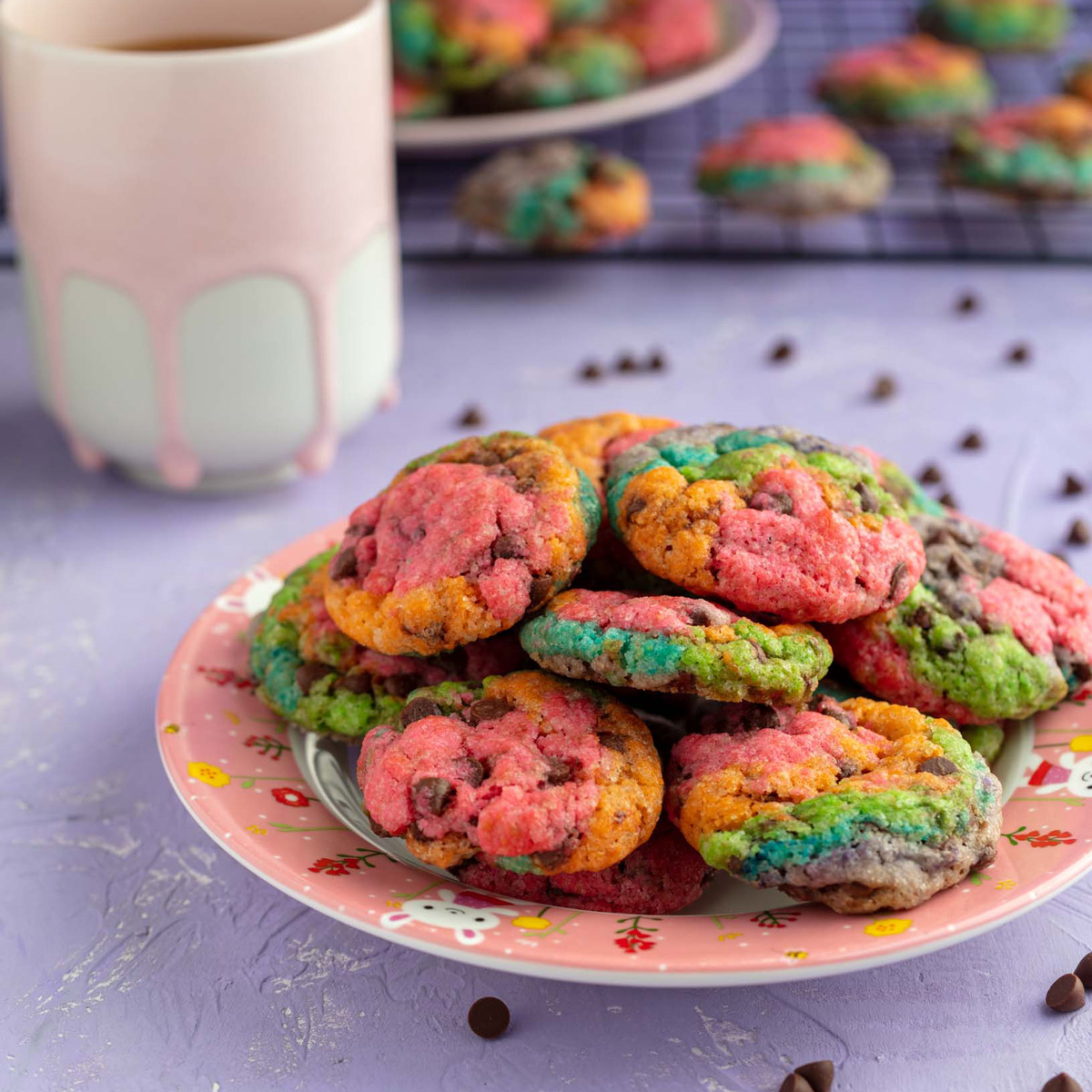 plate of vegan rainbow chocolate chip cookies with a cup of coffee in the background