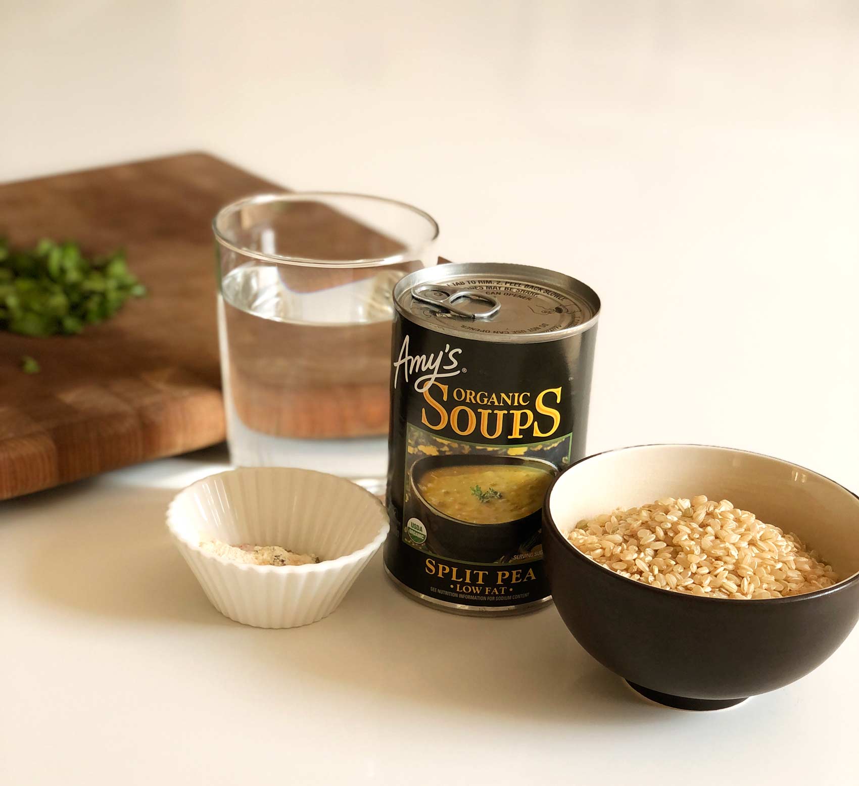 can of split pea soup, glass of water, bowl of brown rice, and a small dish of spices