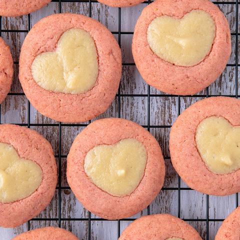 pink strawberry thumbprint cookies with a heart shaped vegan cheesecake in the center