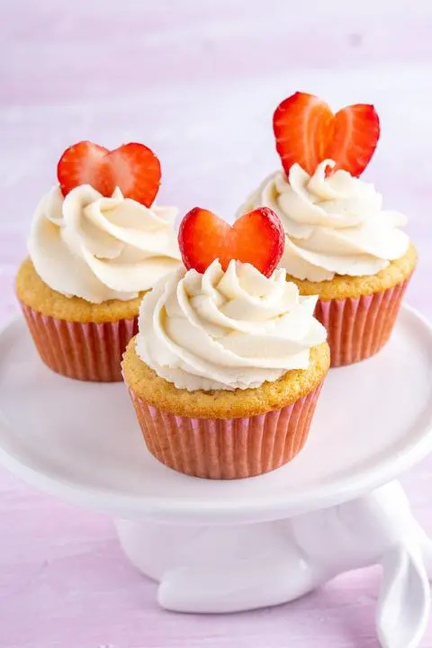 3 frosted and decorated vegan strawberry stuffed cupcakes on a cake stand.