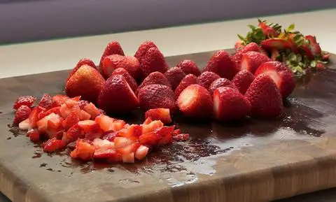 a cutting board with diced strawberries and whole strawberries on it.