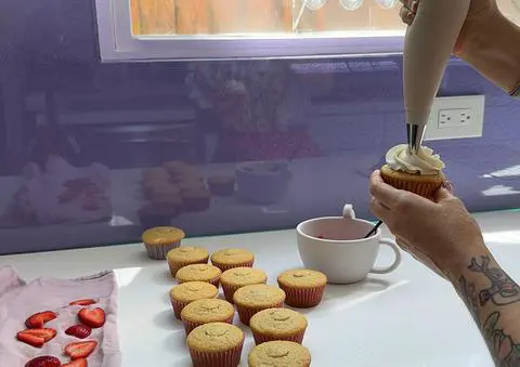 piping vegan vanilla frosting onto the strawberry filled cupcake.