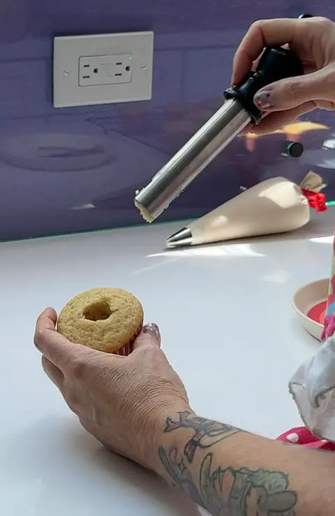 using an apple corer to make a hole in the center of a vegan vanilla cupcake.