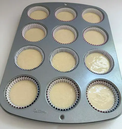 a cupcake pan filled with cupcake papers that have vegan vanilla cake batter in them.