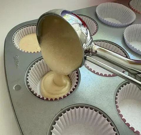 using a large scoop to fill the cupcake papers with vegan vanilla cupcake batter.