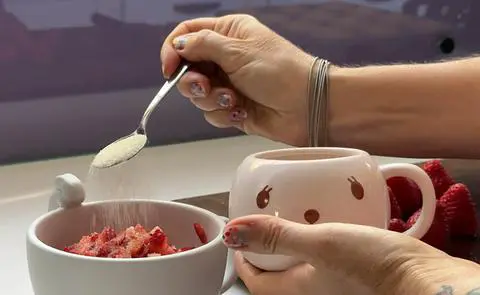 sprinkling vegan sugar over a bowl of strawberry pieces.