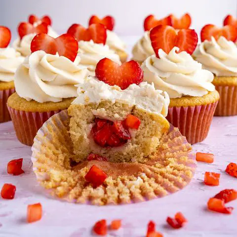 a dozen vegan cupcakes with a bite missing from one showing the fresh strawberry filling inside.