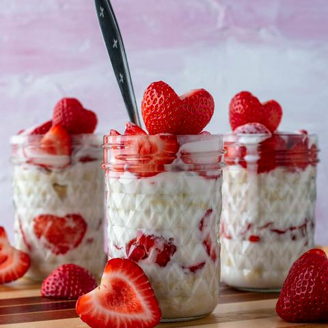 three strawberry shortcake parfaits in mini mason jars with heart shaped strawberries on top of each one