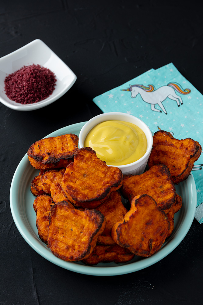 a plate of bear shaped sweet potato tots with a side of dip, a dish of purple salt, and a unicorn napkin