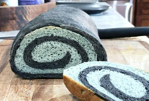 loaf of black and blue swirl bread with one piece sliced showing the spiral