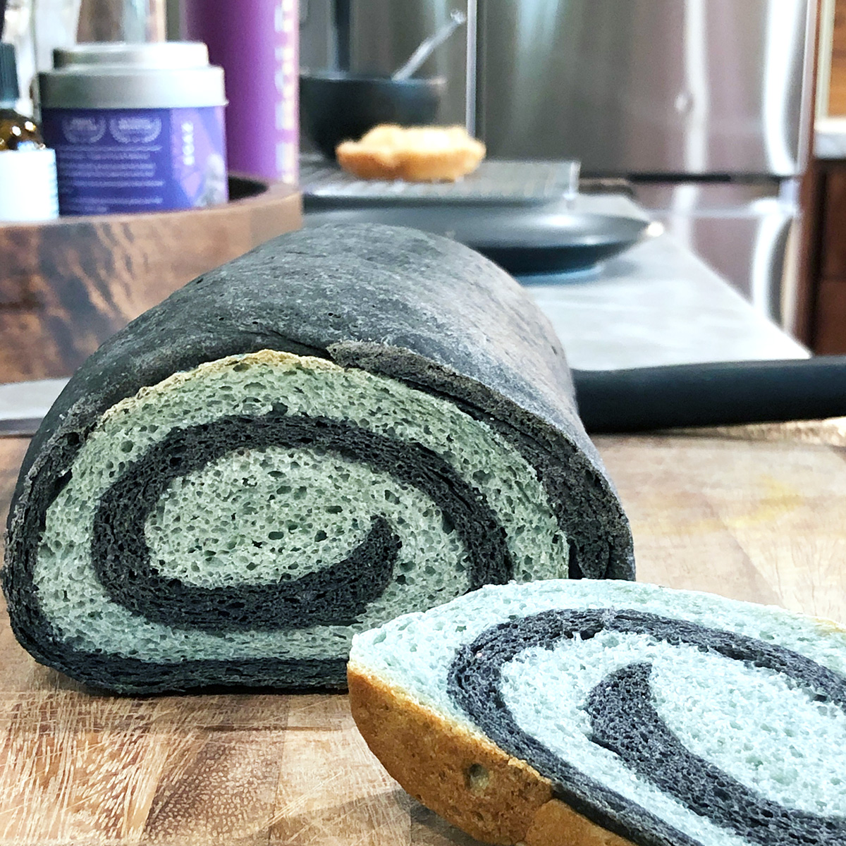 loaf of black and blue swirl bread with one piece sliced showing the spiral