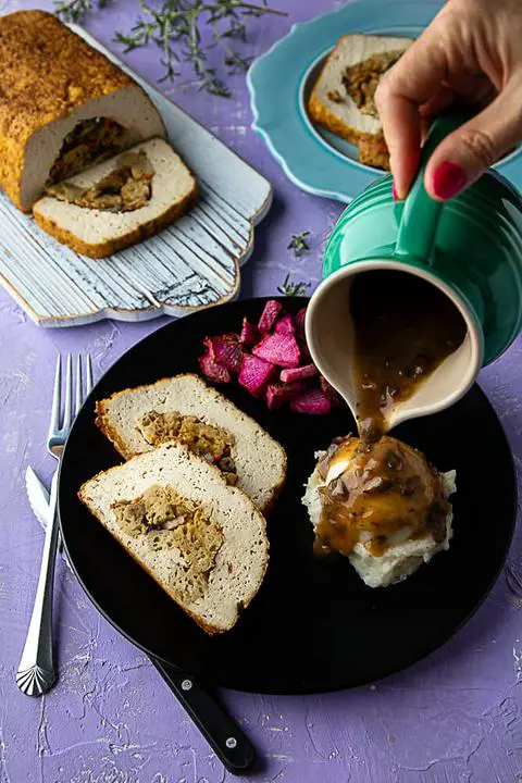 pouring vegan gravy onto Vegan Thanksgiving Tofu Turkey and mashed potatoes