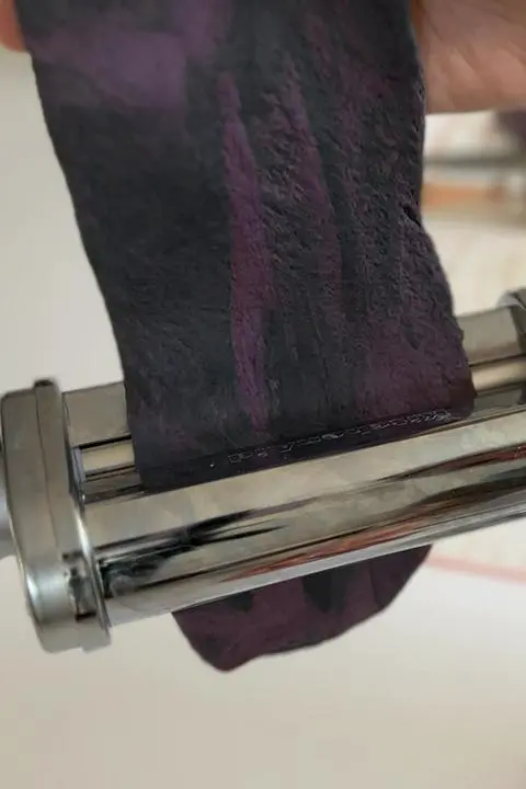 rolling the black and purple striped pasta dough using a kitchenaid pasta roller attachment