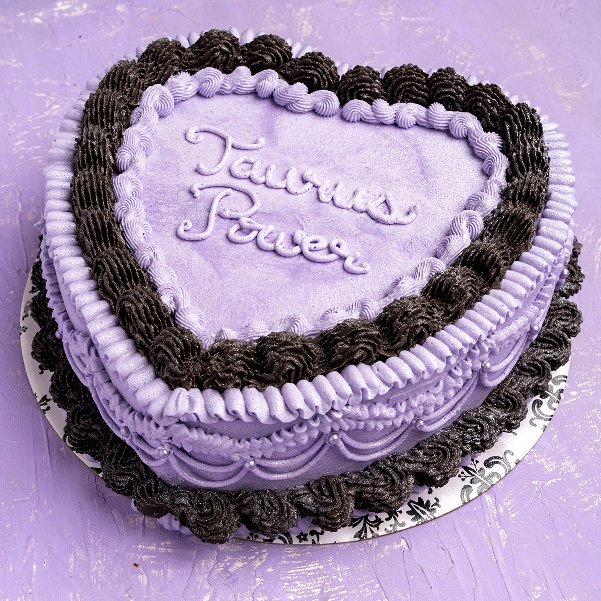 a lavender and black heart shaped vegan cake decorated with a lambeth vintage style.