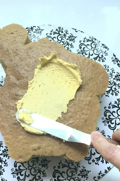 spreading yellow vanilla frosting onto the Pompompurin shaped vegan vanilla cake