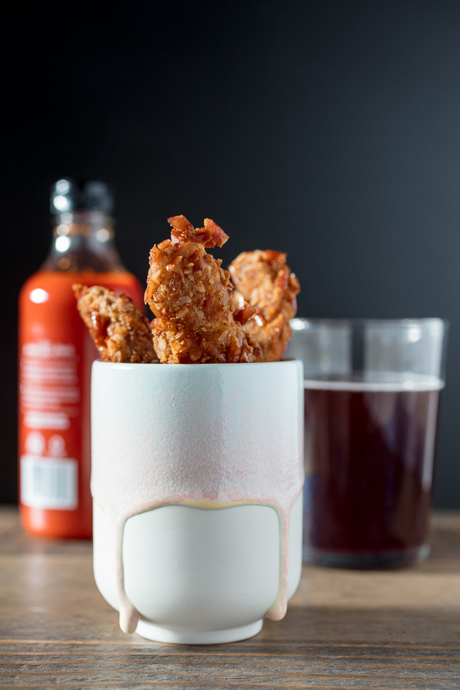 cup of pretzel chicken fries with hot sauce in the background.